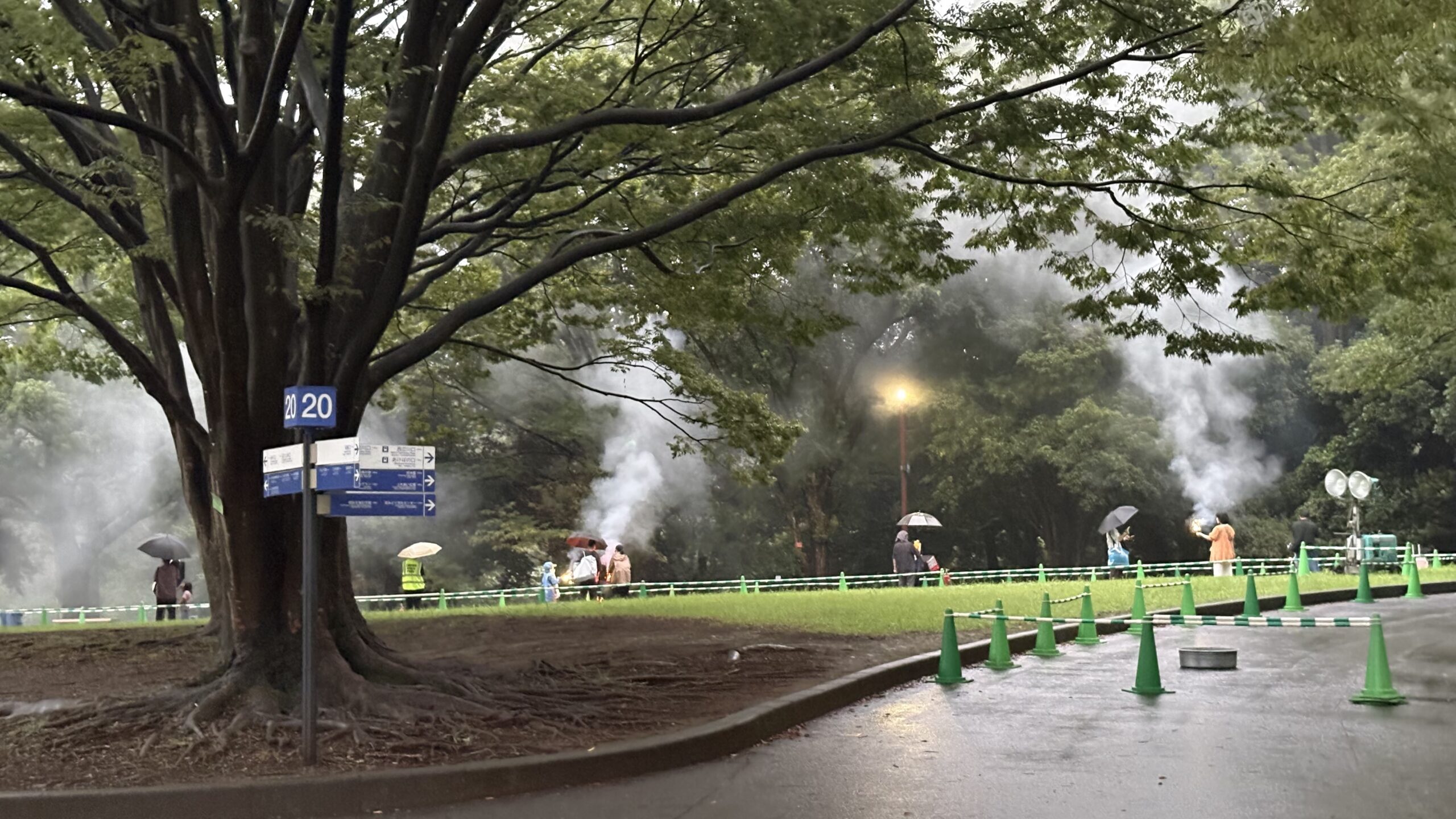 雨のなか、ロープで仕切られた星あかり花火ひろばで手持ち花火を楽しむ来場者と立ちのぼる煙
