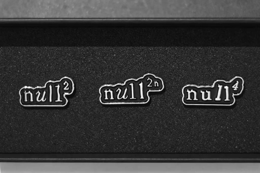 黒いケースに並ぶ3つのメタルピンバッジ。左からnull²、null²ⁿ、null⁴のロゴ