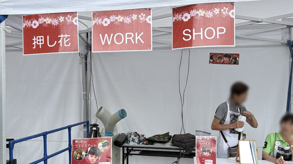 ブース内に掲げられた「押し花」「WORK」「SHOP」の3つのサインと、体験を待つ来場者