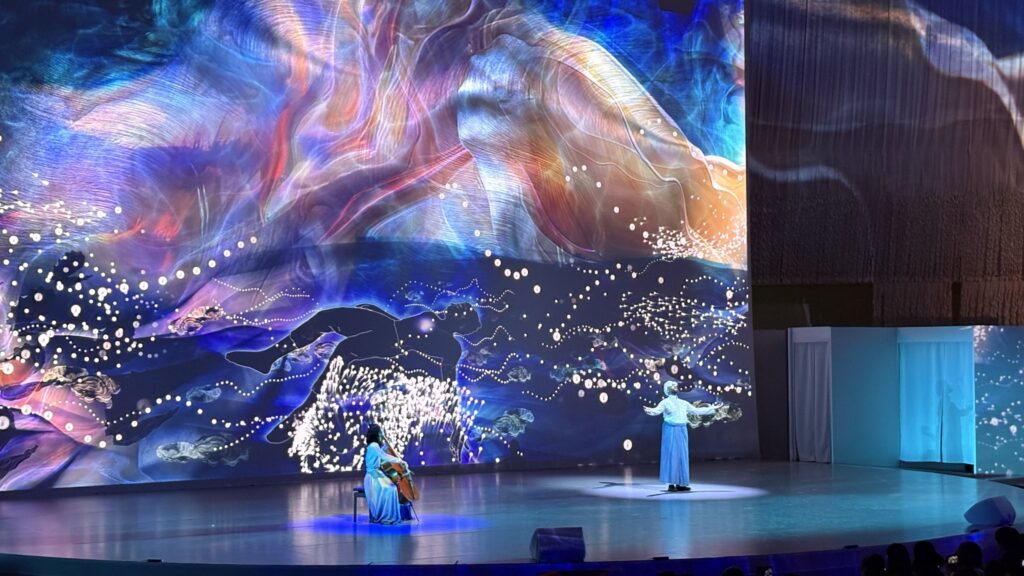 大型映像の前でチェロの演奏とパフォーマンスが行われる舞台