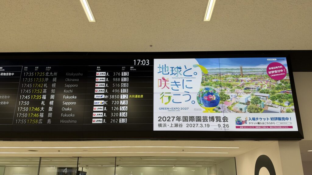 第1ターミナル到着ロビーの到着便案内板と、横のGREEN×EXPO 2027のデジタル広告