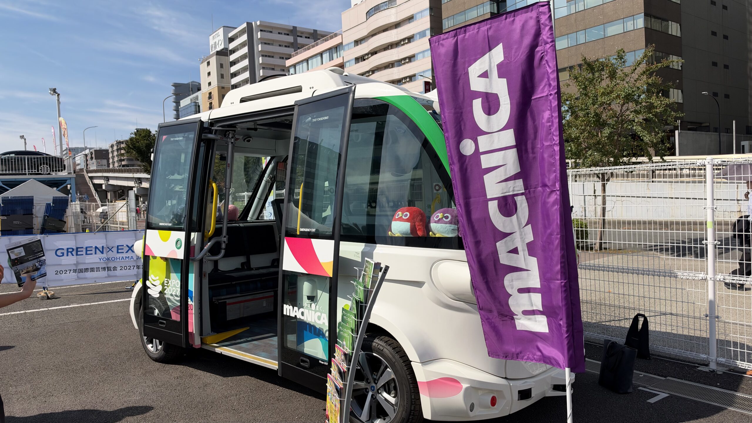 扉が開いたマクニカの自動運転EVバスの側面とMACNICAの幟