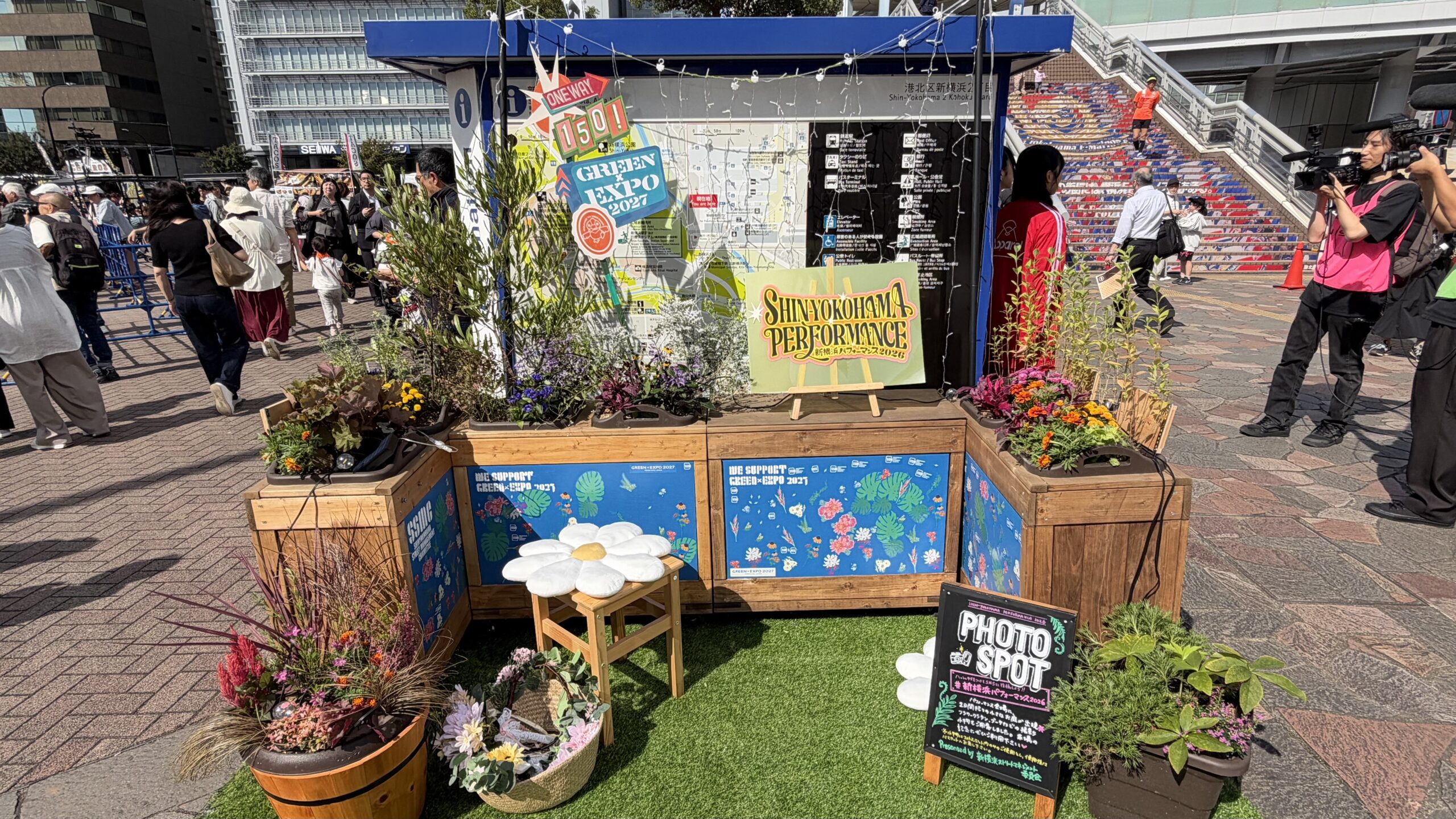 駅前案内所の前のフォトスポット。WE SUPPORT GREEN×EXPO 2027のプランターと花のクッション