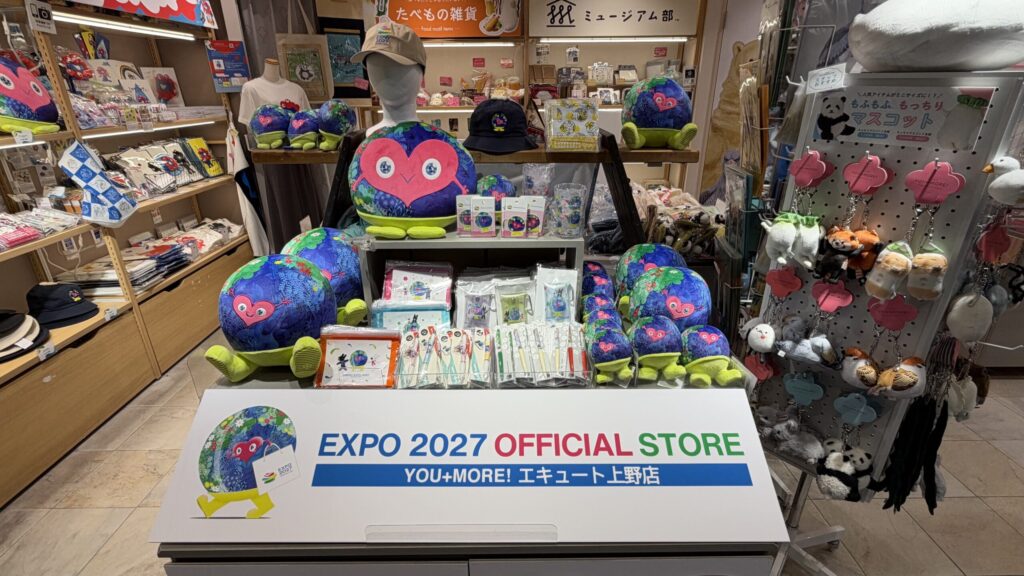 EXPO 2027 OFFICIAL STOREの看板が付いた台に、クッションやぬいぐるみが並ぶ