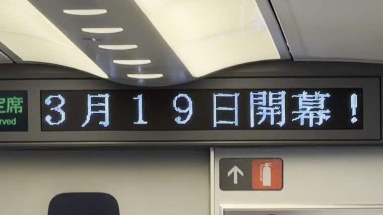 新幹線の車内表示板に流れる「3月19日開幕！」の文字