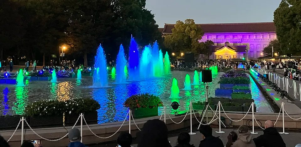 夜の上野恩賜公園の噴水広場で、青や緑にライトアップされた噴水