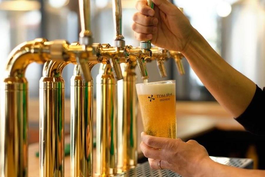 金色のタップからTDM 1874 Breweryのロゴ入りグラスにビールを注ぐ様子