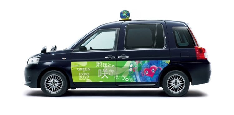 車体の横にGREEN×EXPO 2027のロゴとトゥンクトゥンクのラッピングをした濃紺のタクシー。屋根にトゥンクトゥンクの立体装飾